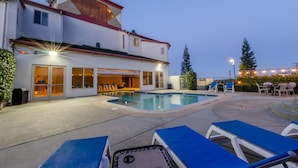 A modern building with a swimming pool, outdoor seating, and a well-lit entrance.