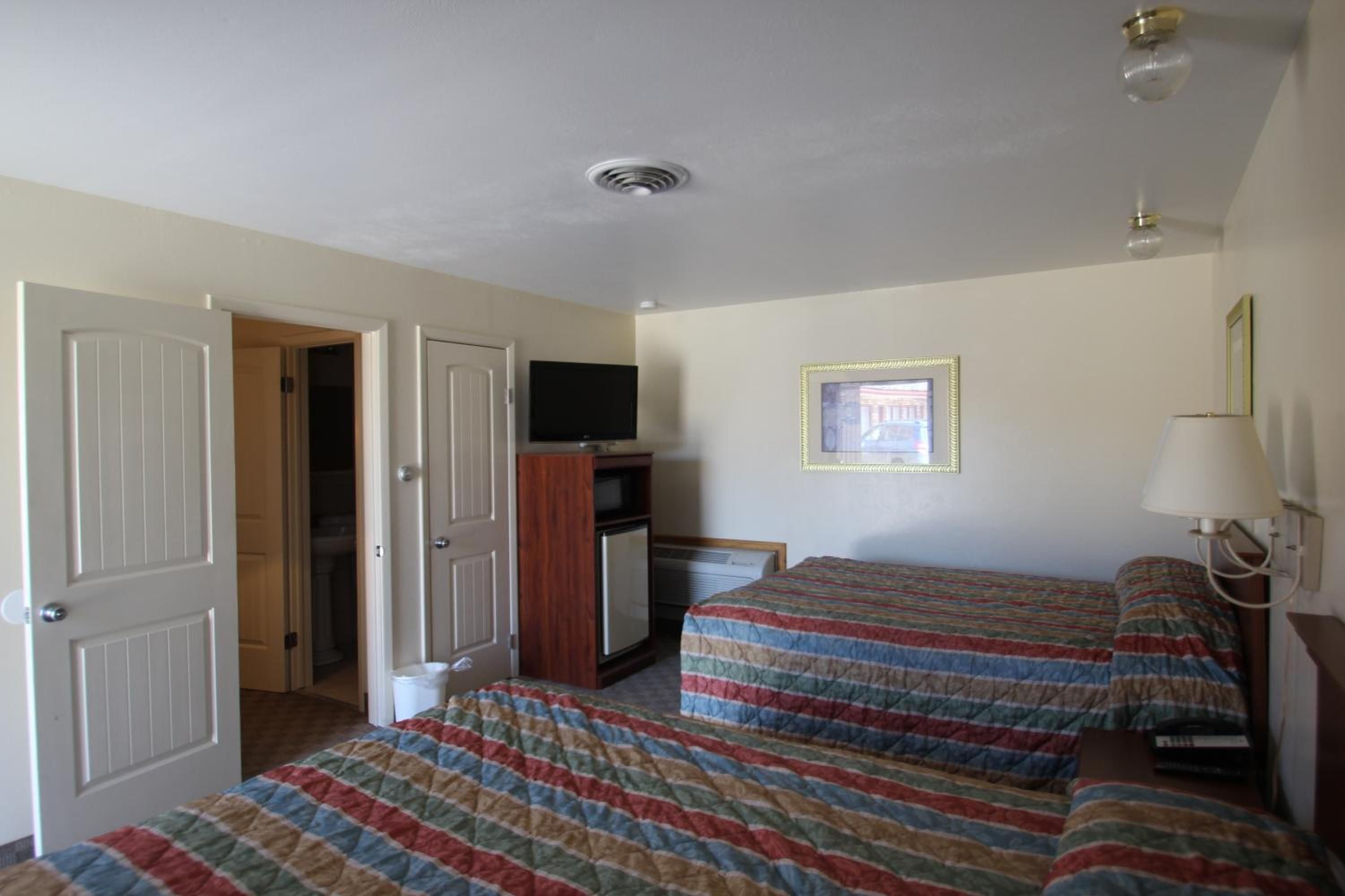 Una habitación con dos camas, un televisor, un ventanal pequeño y una puerta que da a un baño.