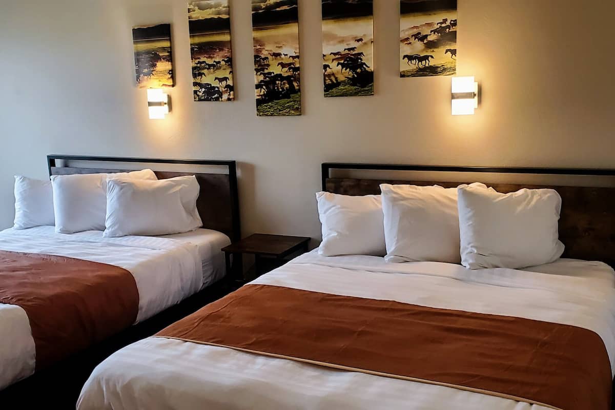 A hotel room with two beds, a chair, and wall-mounted artwork.