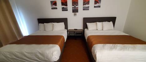Habitación de hotel con dos camas, una mesita de noche, una lámpara de pared y una ventana con cortinas.