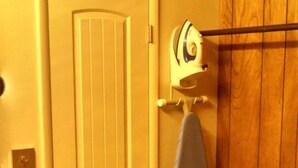 Un baño con una puerta blanca, un perchero con toalla, un banco de madera y una cafetera.