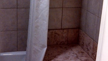 A shower area with a white curtain, tiled walls, and a small step leading to a bathtub.