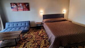 Une chambre d’hôtel avec un lit, un canapé, une petite table et un tapis à motifs.