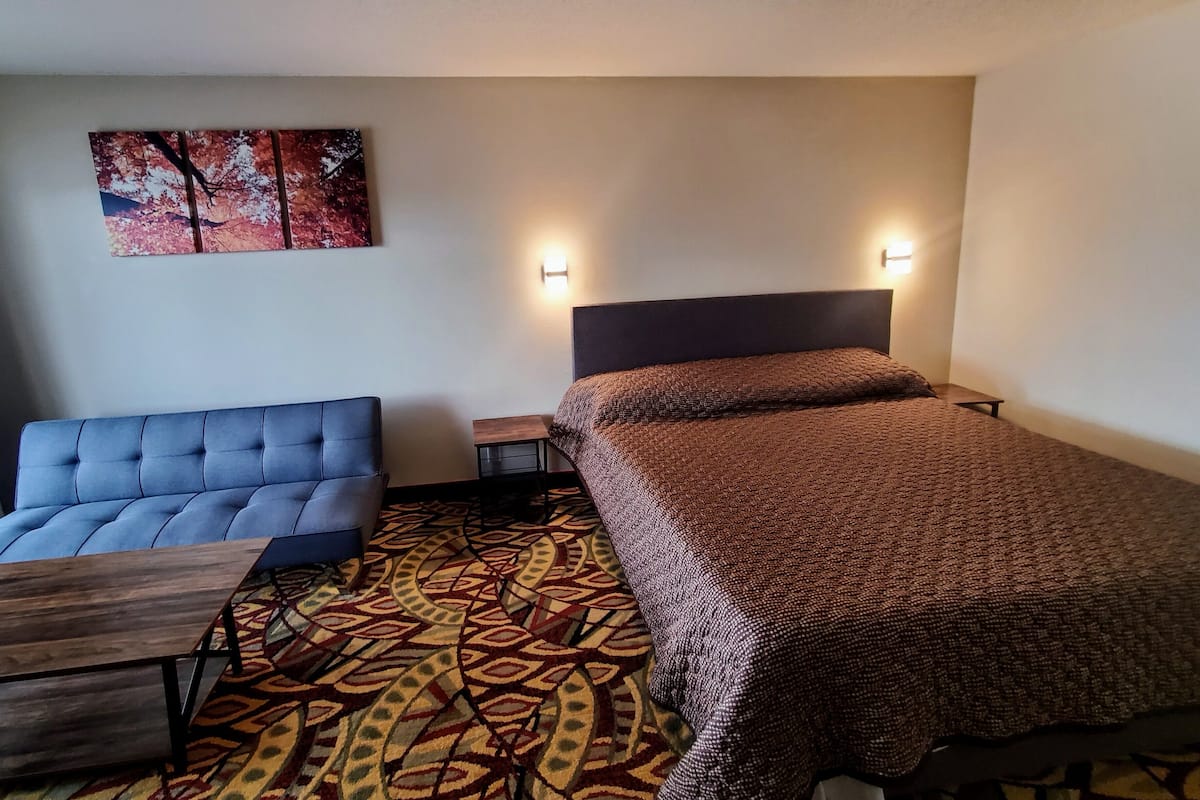A hotel room with a bed, a sofa, a small table, and a patterned carpet.