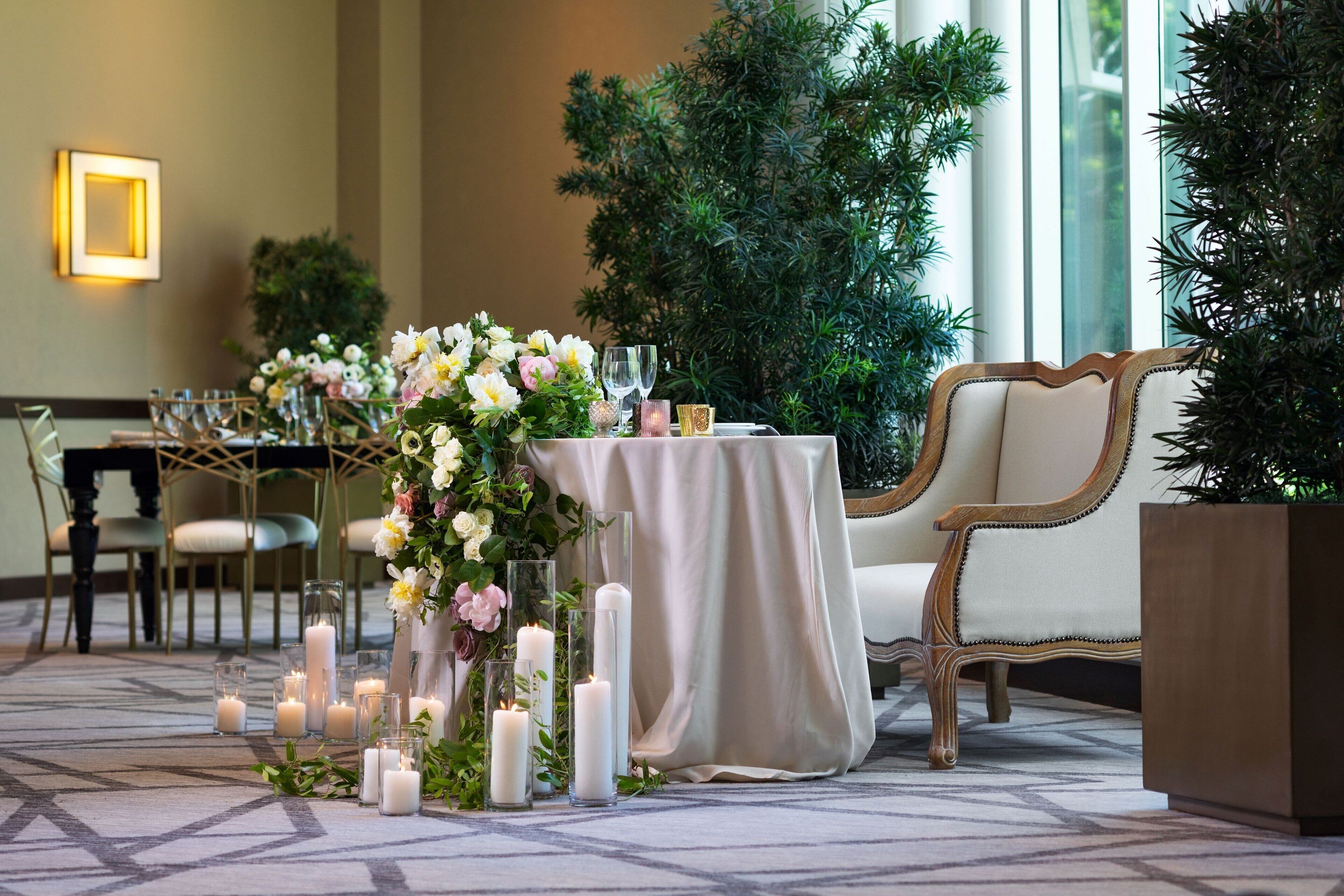 A well-lit indoor setting with a table set for a formal event, surrounded by chairs and a decorative floral arrangement.