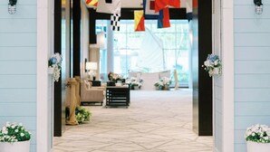 A hallway with a blue wall, white trim, and a geometric patterned floor. There are potted plants on either side and a checkered flag hanging from the ceiling. - The Westin Edina Galleria (Edina)