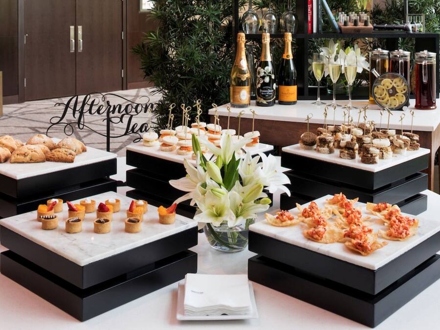 A buffet table with various desserts and beverages, surrounded by a decorative setting with flowers and a sign that reads "Afternoon Tea".