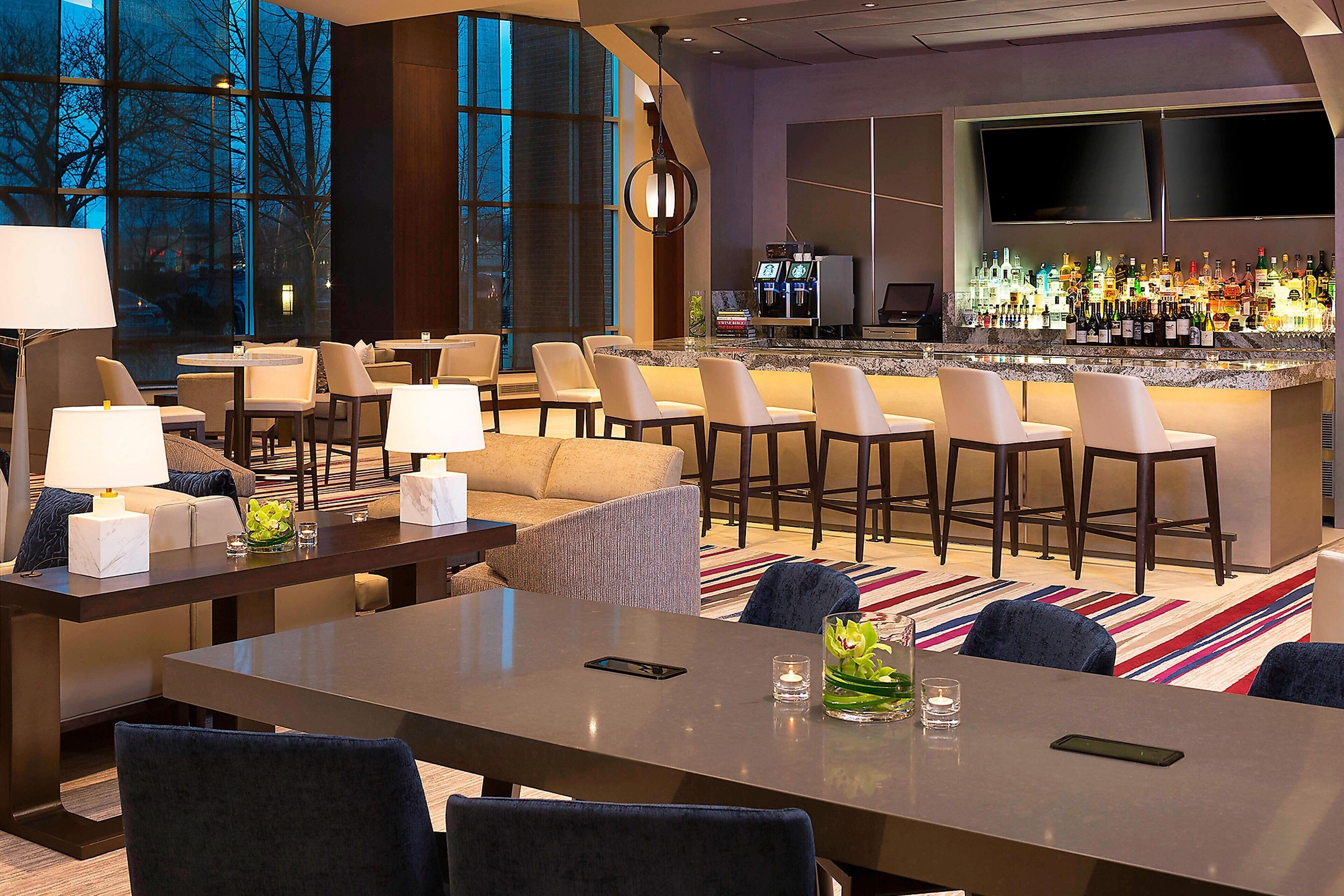 A hotel lobby with a bar area, seating arrangements, and a large window providing a view of the outside.