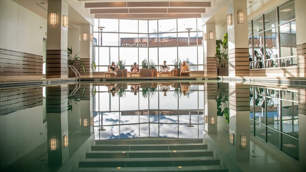 A spacious indoor pool area with clear reflections, large windows, and a seating area with plants. - The Westin Edina Galleria (Edina)