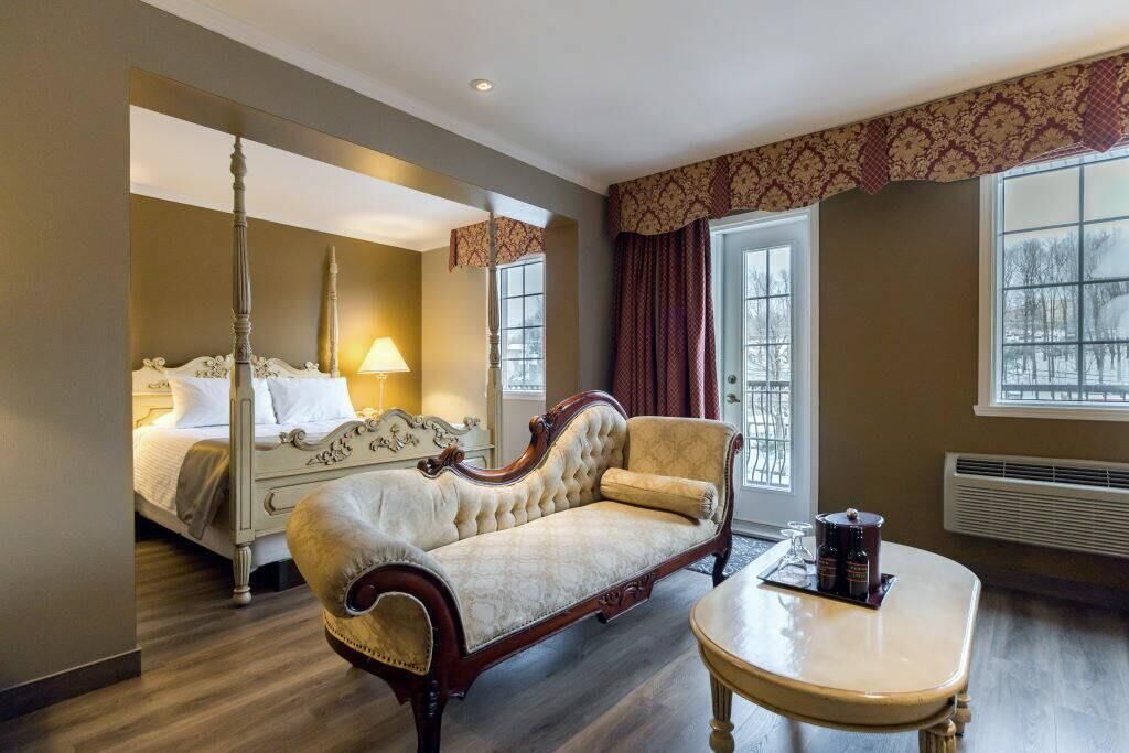 Ein Hotelzimmer mit Himmelbett, einer Sitzecke, einem runden Tisch und einem großen Fenster mit Vorhängen.