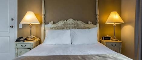 A neatly made bed with a classic headboard, two bedside tables with lamps, and a door to the left.