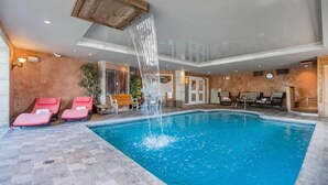 An indoor swimming pool with a waterfall feature, surrounded by red lounge chairs and wooden benches. - St Christophe Hotel & Spa, an Ascend Collection Hotel (Granby)