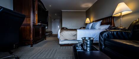 A hotel room with a bed, a desk, a chair, a leather sofa, and a minibar.