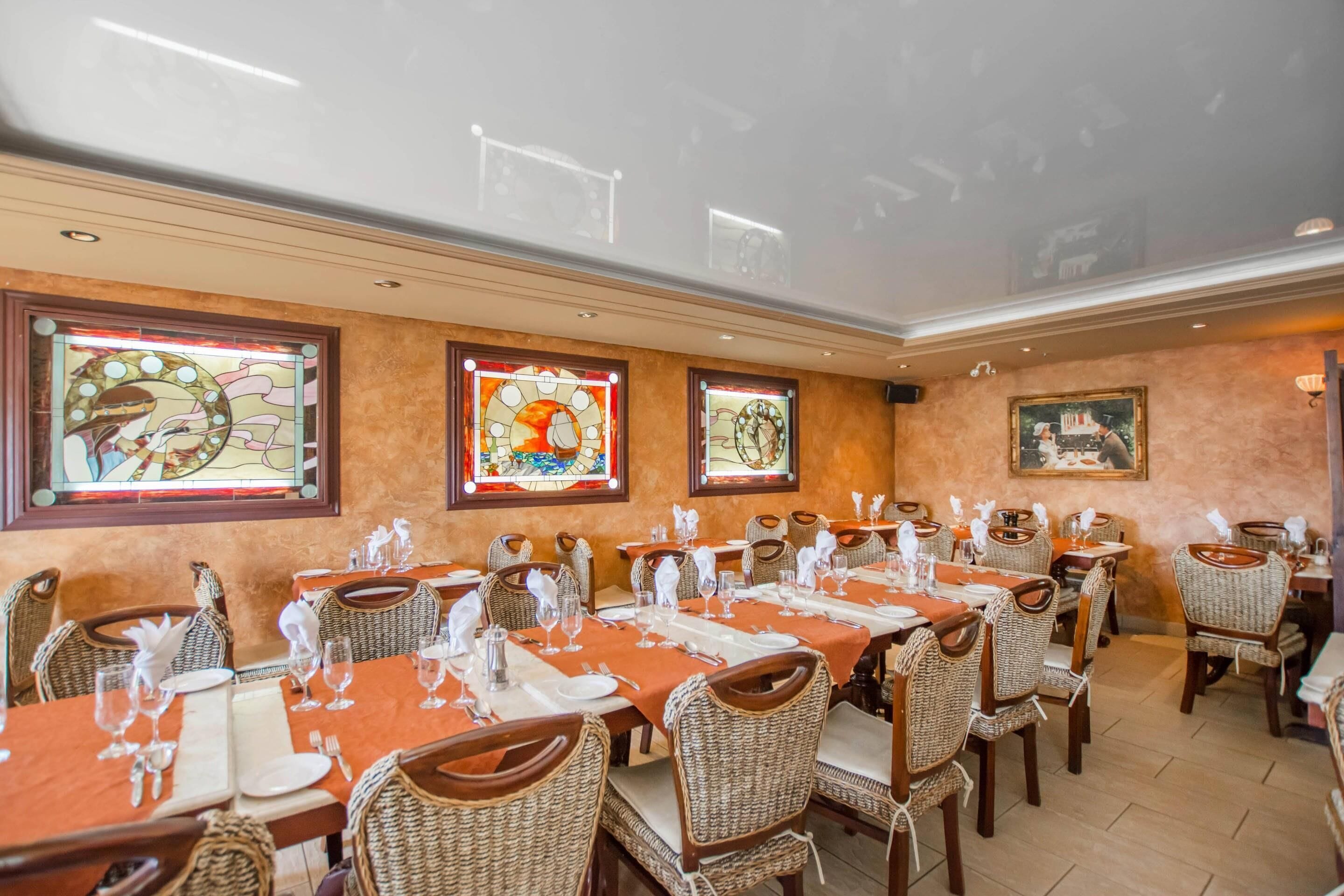 A dining area with tables set for service, wicker chairs, and stained glass windows.