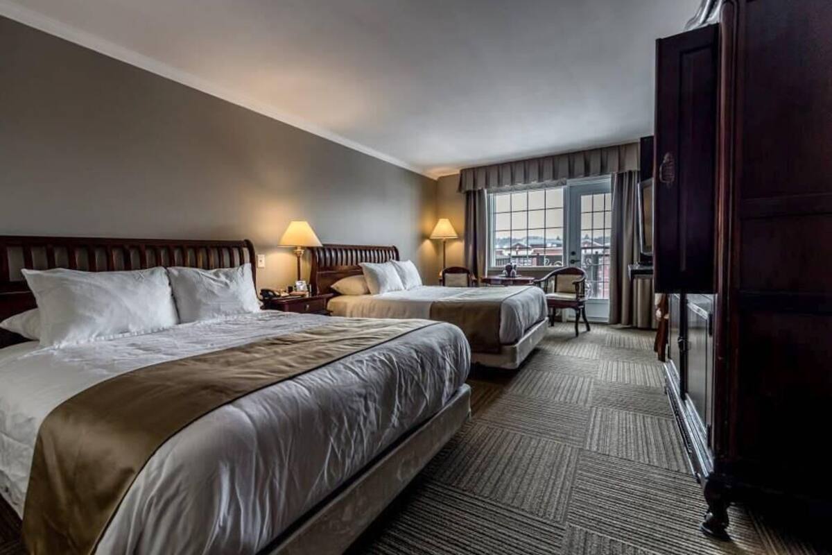 Habitación de hotel con dos camas, un ventanal grande y vistas a la ciudad.
