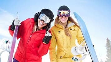 Two people in ski gear, one holding a ski pole and the other a snowboard, standing in a snowy landscape.