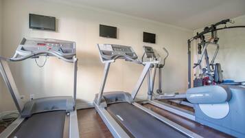 Three treadmills in a room with a wooden floor, a wall-mounted TV, and a weight machine.