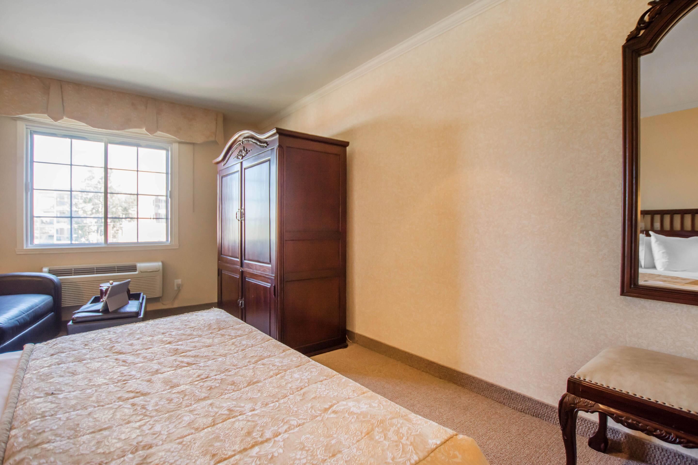 A bedroom with a large bed, a wardrobe, a bench, a desk, and a window with a view.