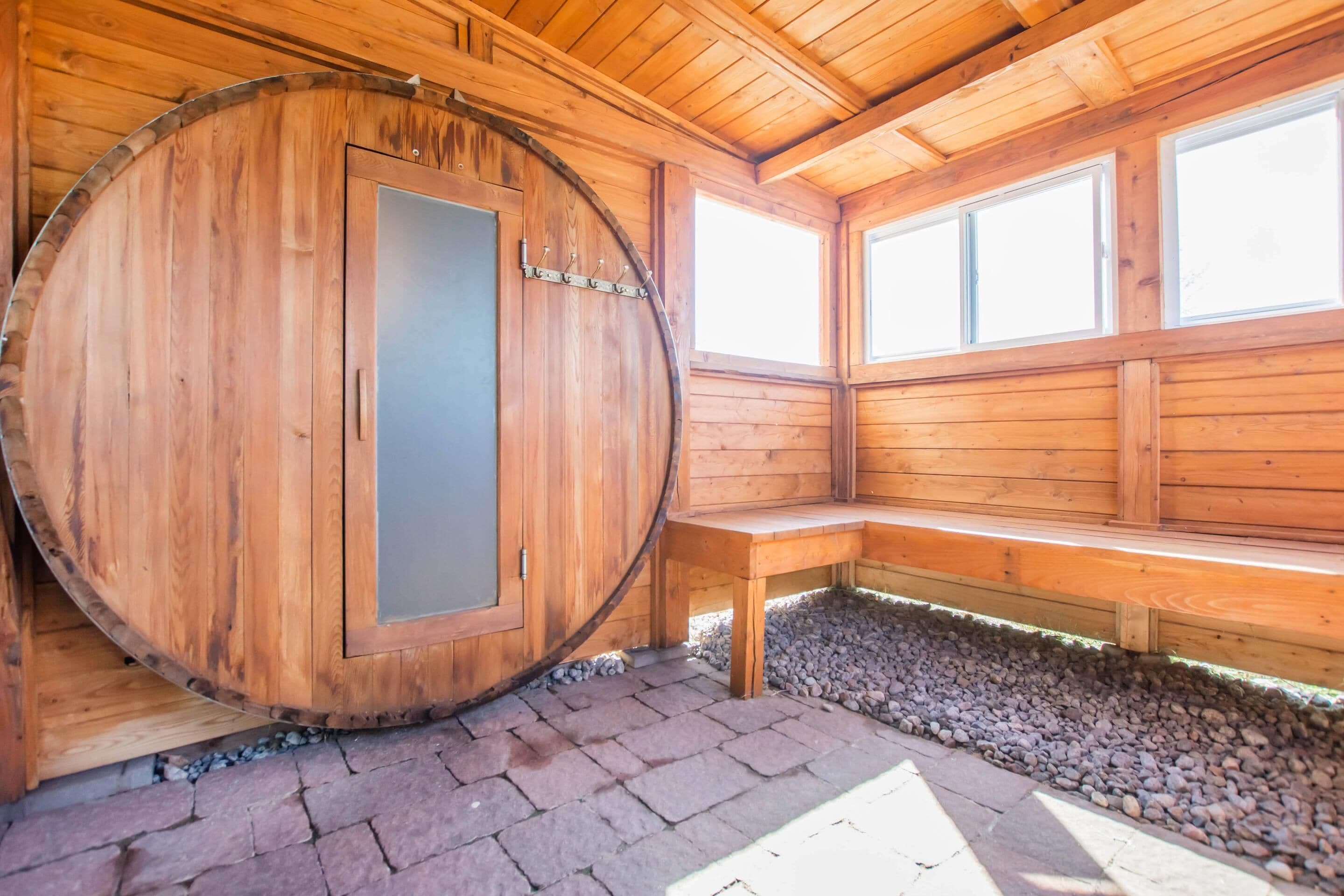 Eine Holzsauna mit einer großen, runden Tür, einer Sitzbank und einer Wand mit Fenstern.