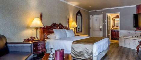 A hotel room with a large bed, two bedside lamps, a wooden nightstand, a small table with a glass, and a mirror above the bed.