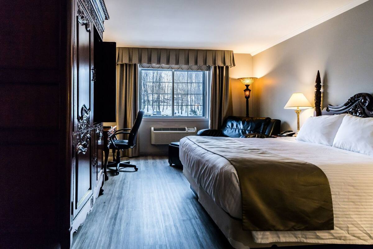 Habitación de hotel con cama, escritorio, silla, lámpara y ventana con cortinas.