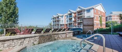 A swimming pool with a stone wall and metal railings, surrounded by lounge chairs and a brick pathway.