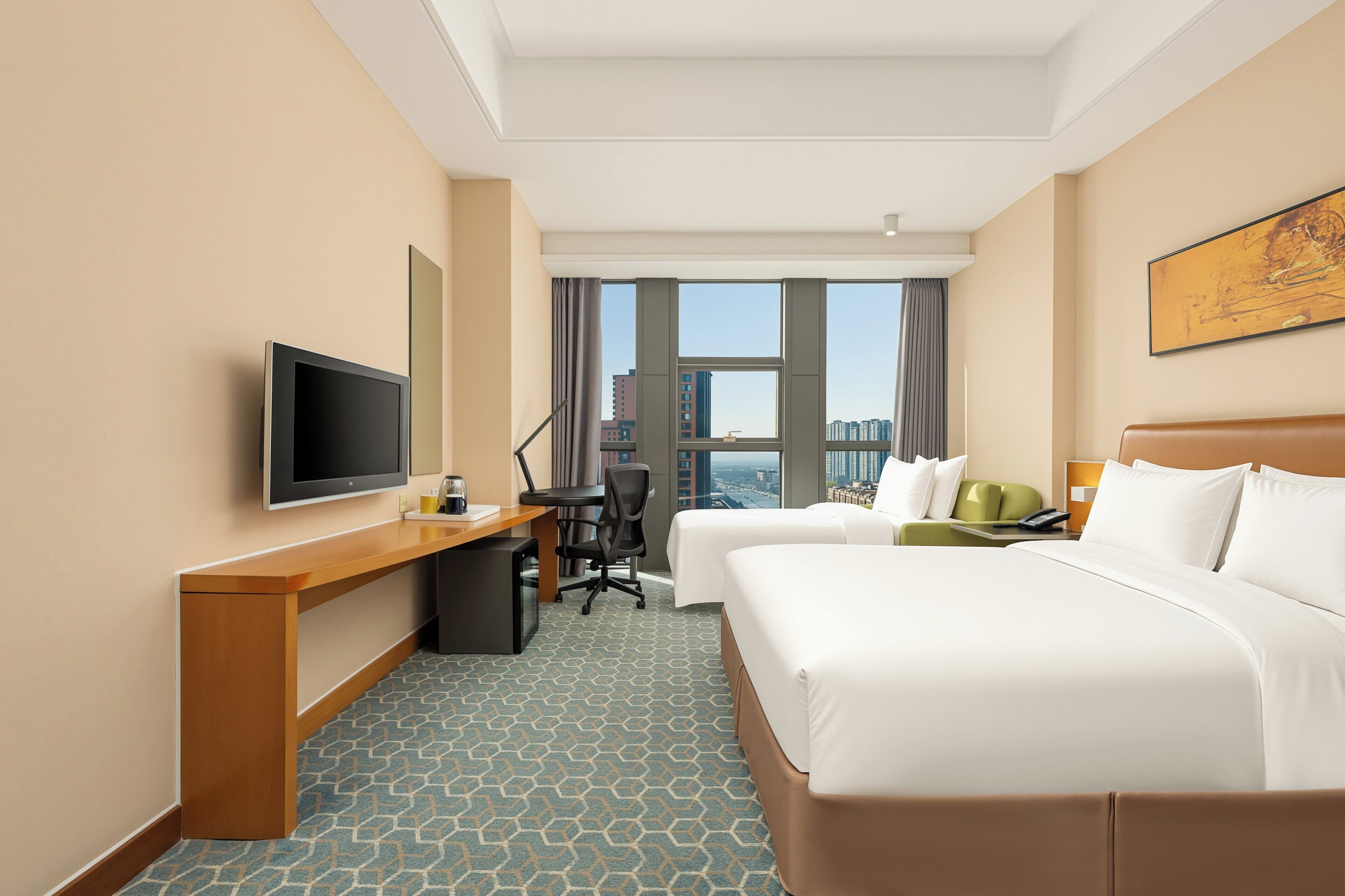 A hotel room with a bed, a desk with a computer, a television, and a window with a city view.