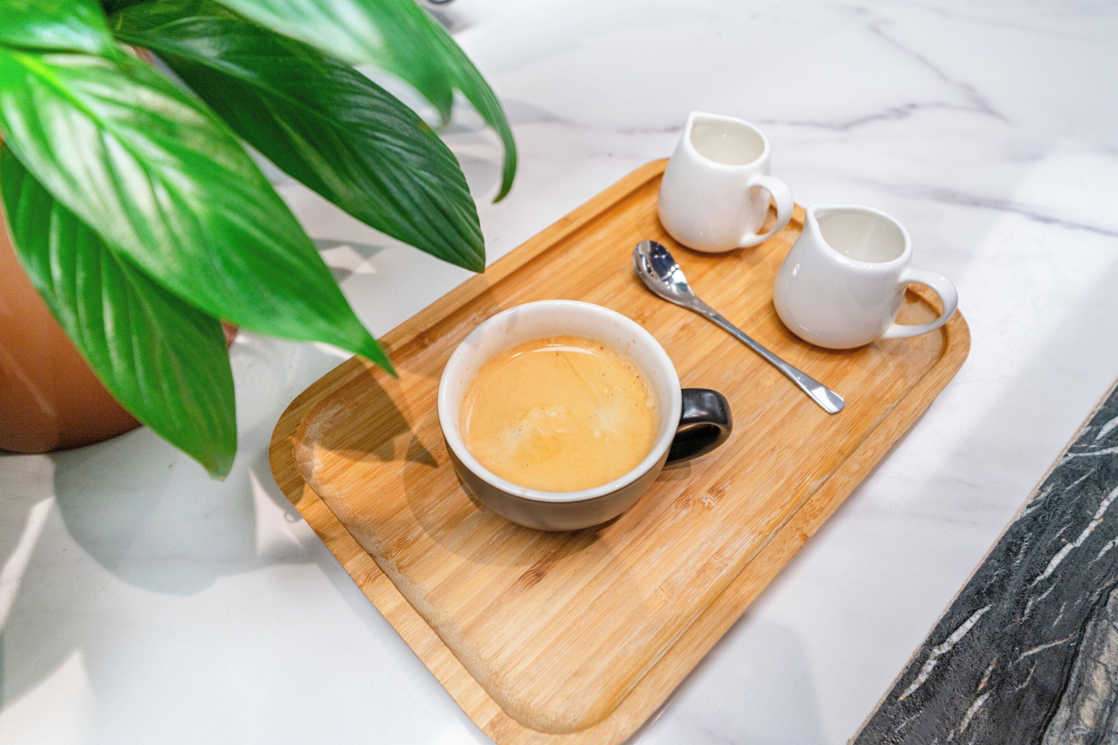 Una bandeja con una taza de café, dos tazas blancas pequeñas y una cuchara sobre una tabla de madera.