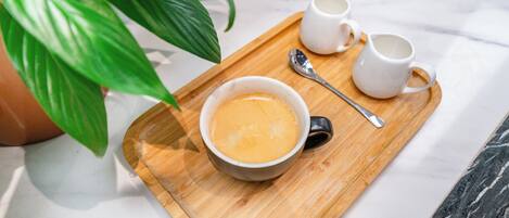 Una bandeja con una taza de café, dos tazas blancas pequeñas y una cuchara sobre una tabla de madera.