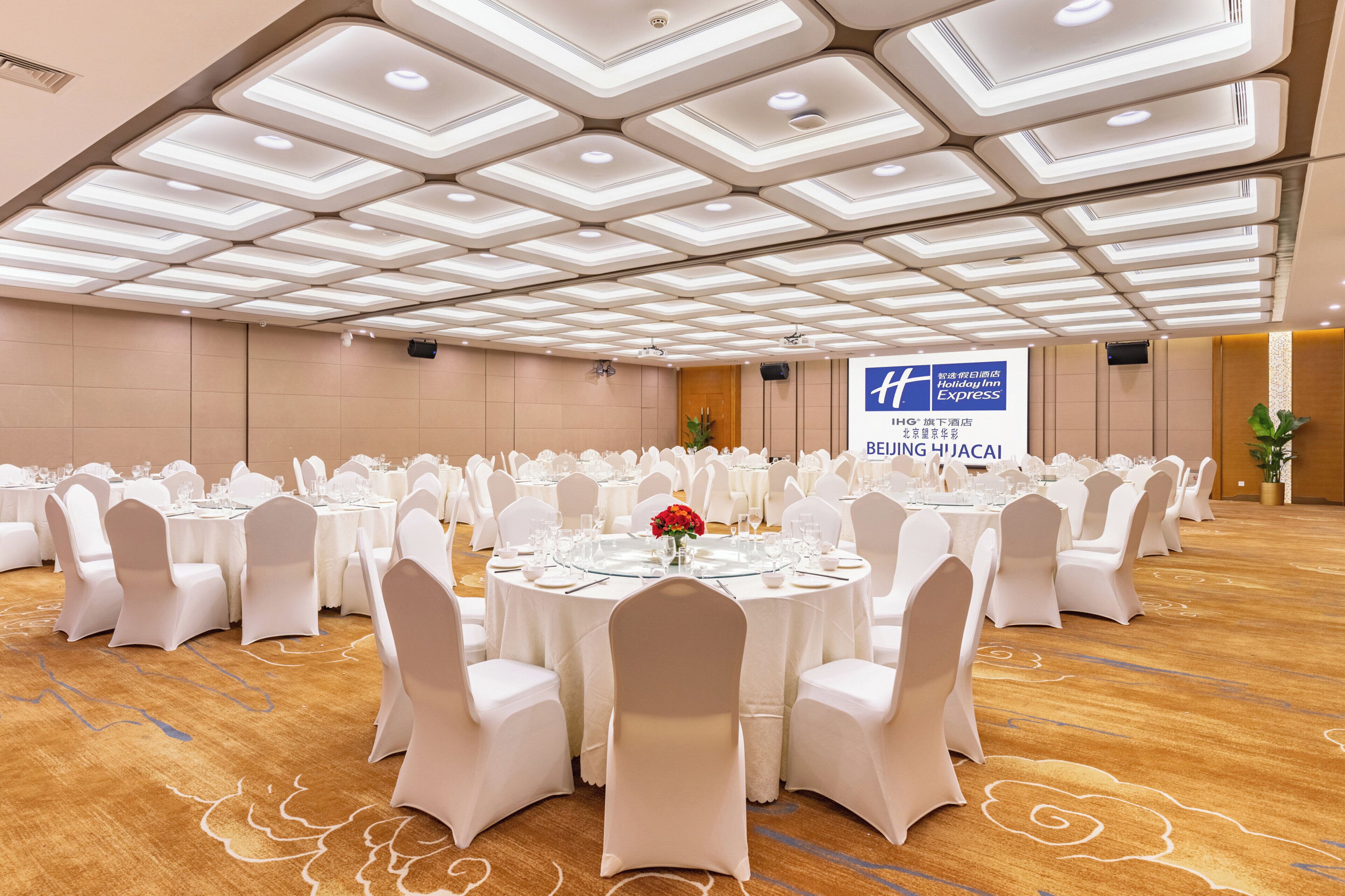 A large conference room with round tables, white chairs, and a ceiling with recessed lighting.