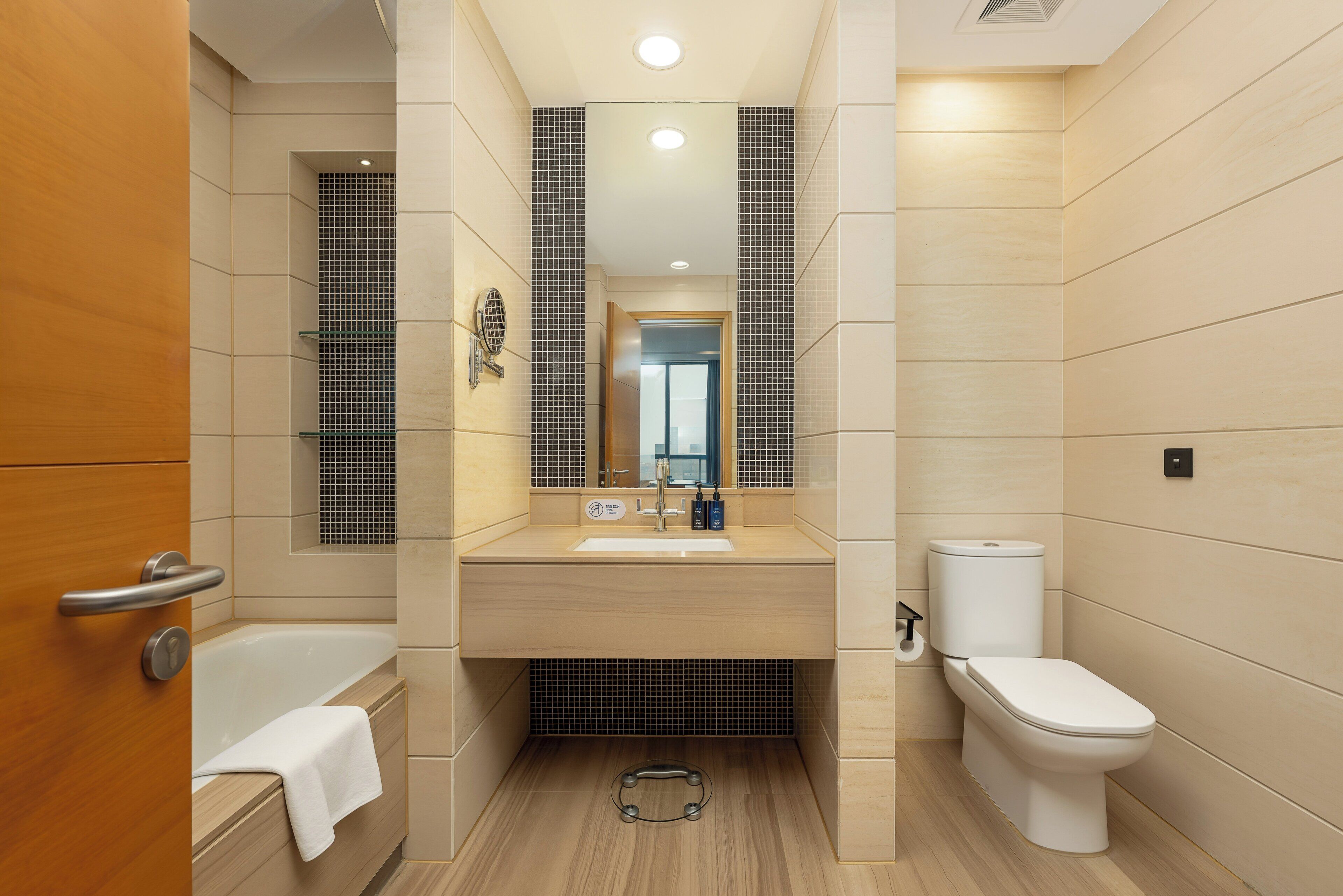 A modern bathroom with a bathtub, sink, and toilet, featuring a wooden vanity and tiled walls.