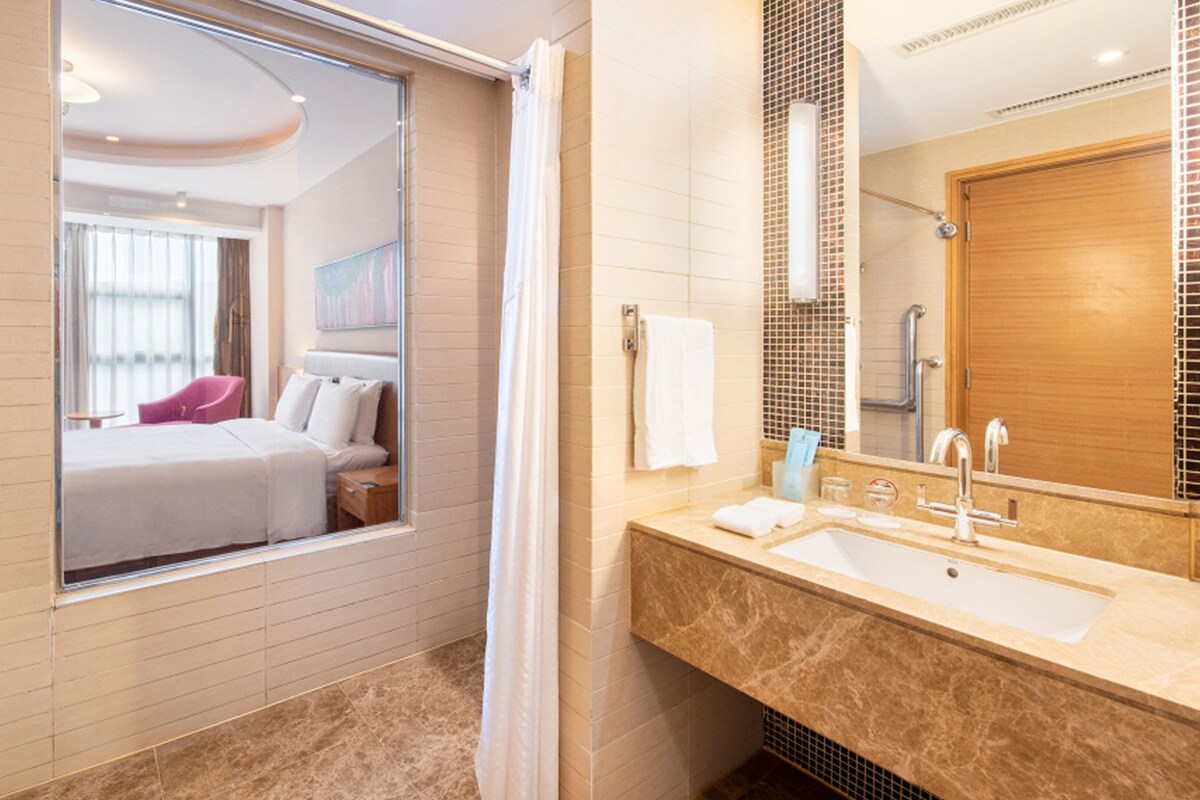A hotel bathroom with a shower, a sink, and a large mirror.
