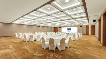 Un salón de conferencias con mesas redondas, sillas blancas y una pantalla grande.