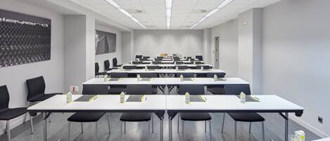 Un salón de conferencias con varias mesas, sillas y botellas de agua.