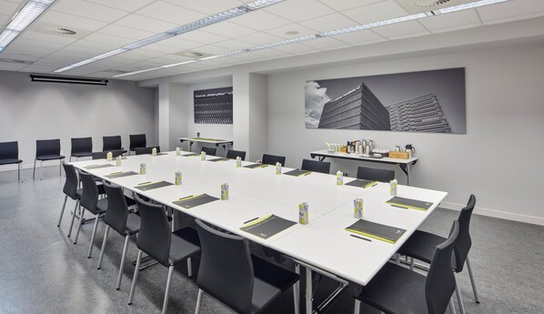Un salón de conferencias con una larga mesa, sillas negras y una pantalla de proyector.