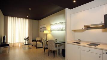 A modern hotel room with a dining area, a flat-screen TV, a lamp, and a large window with curtains.