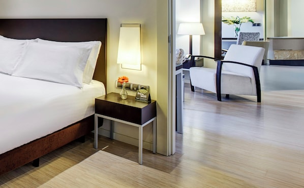 Habitación de hotel con cama, mesita de noche con lámpara, una silla y escritorio con cartel que indica wifi gratuito.