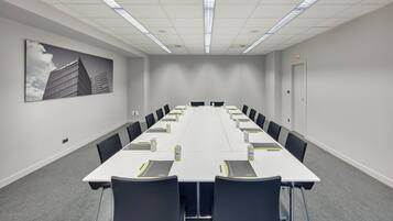 Uma sala de conferências com uma mesa comprida, cadeiras e um projetor.