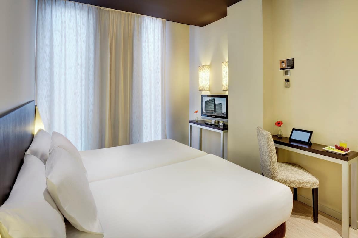 Habitació d'hotel amb un llit gran, un escriptori amb un ordinador i una televisió.