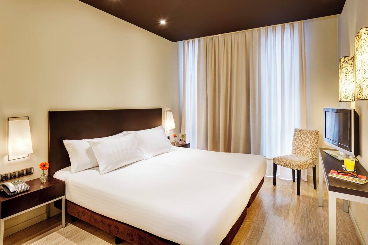 A hotel room with a large bed, a desk with a computer, a chair, and a TV.