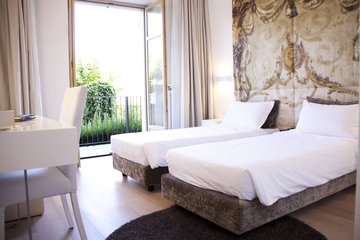 Une chambre d’hôtel avec deux lits, un bureau et une vue sur la verdure environnante.