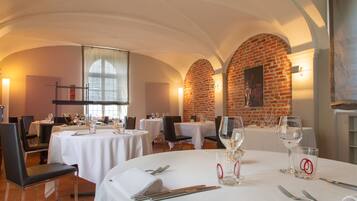 A restaurant with round tables, white tablecloths, and brick walls.