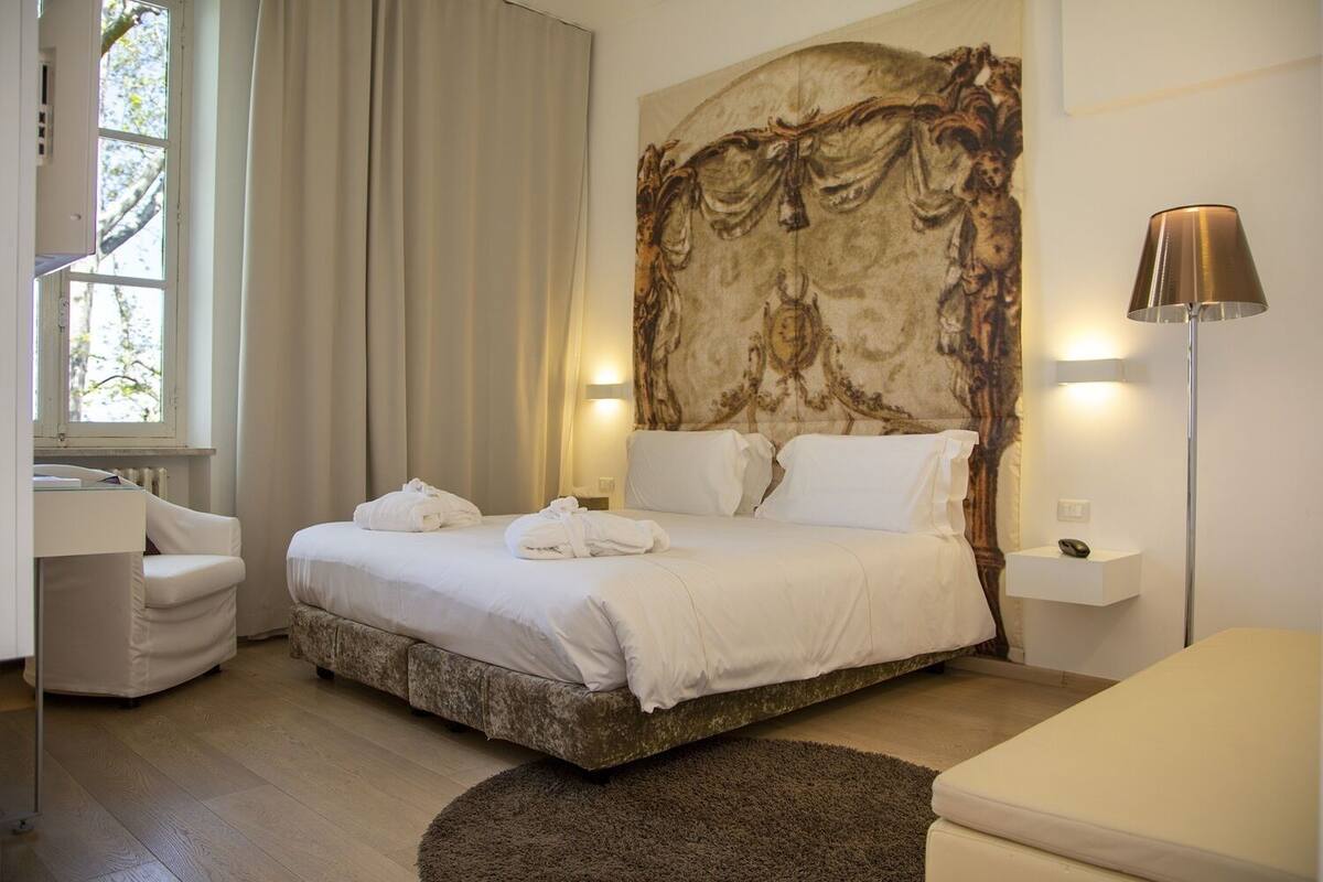 Une chambre à coucher avec un grand lit, une table de chevet, une lampe et une fenêtre avec des rideaux.