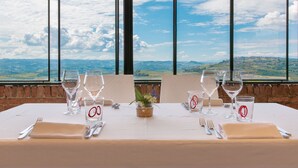 A table set for two with wine glasses, water glasses, and cutlery, overlooking a scenic landscape.