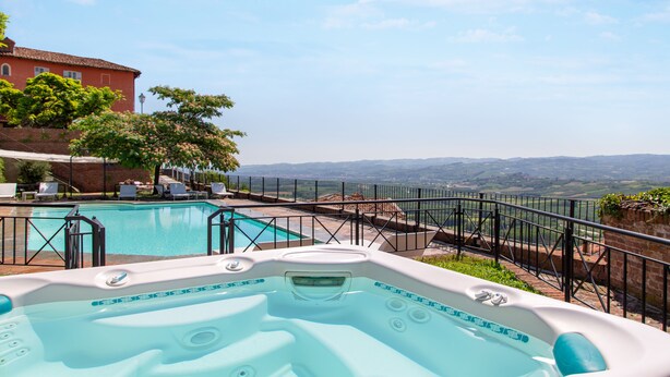 A rooftop pool with a hot tub, surrounded by a fence, and overlooking a scenic landscape.