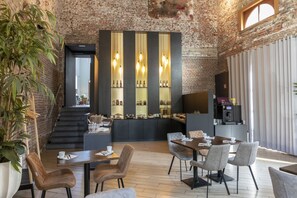 A modern interior with a brick wall, a staircase, a bar area with bottles, and a dining area with chairs and tables. - Eburon Hotel - Different Hotels (Tongeren)