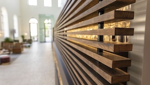 A modern interior with a wooden slatted bench along a wall, a hallway with natural light, and a visible door leading to another area. - Eburon Hotel - Different Hotels (Tongeren)