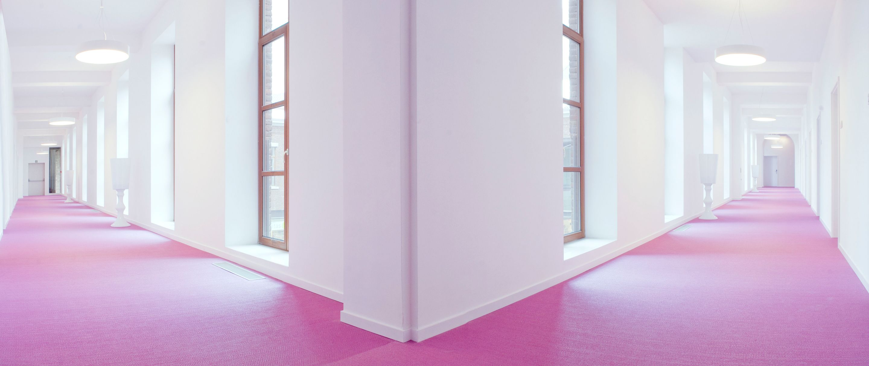 Een lange, smalle gang met witte muren en een roze vloerkleed.