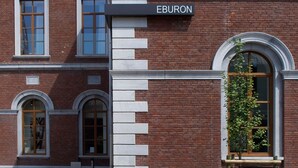 A brick building with a sign reading "EBURON" and a small table with a plant in front. - Eburon Hotel - Different Hotels (Tongeren)