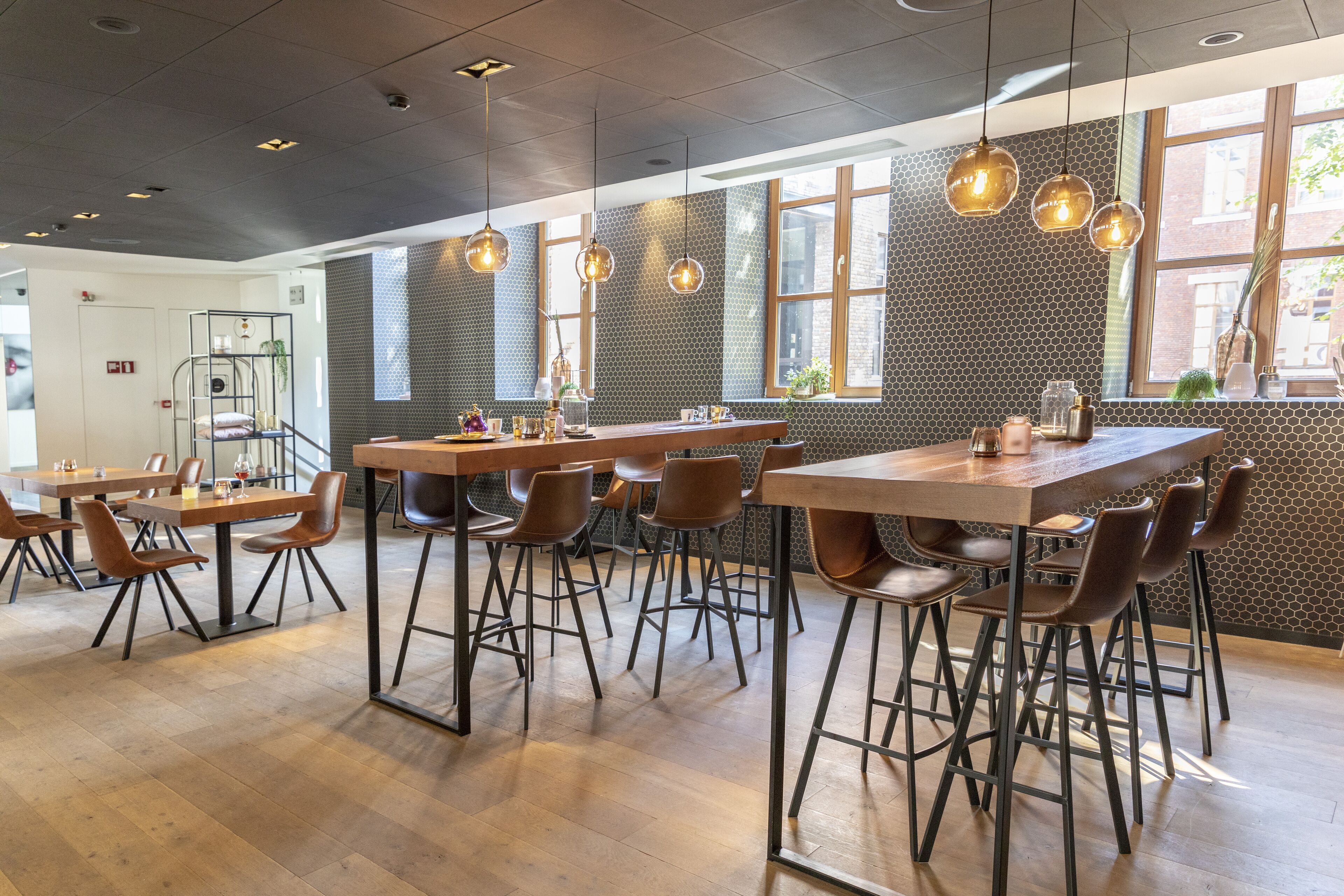 Un café moderno con mesas y sillas de madera, iluminación colgante y una pared de ladrillo con ventanas.